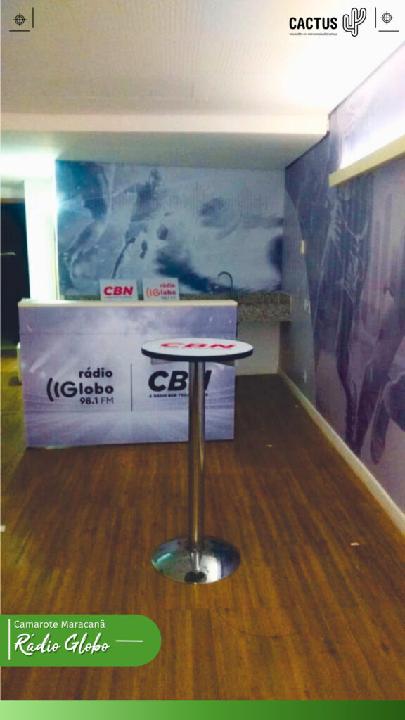 Copa (cozinha) no canto do camarote da rede globo no maracanã com paredes adesivadas, balcão adesivado com logos da rádio globo e CBN e uma mesa bistrô adesivada com logo da CBN